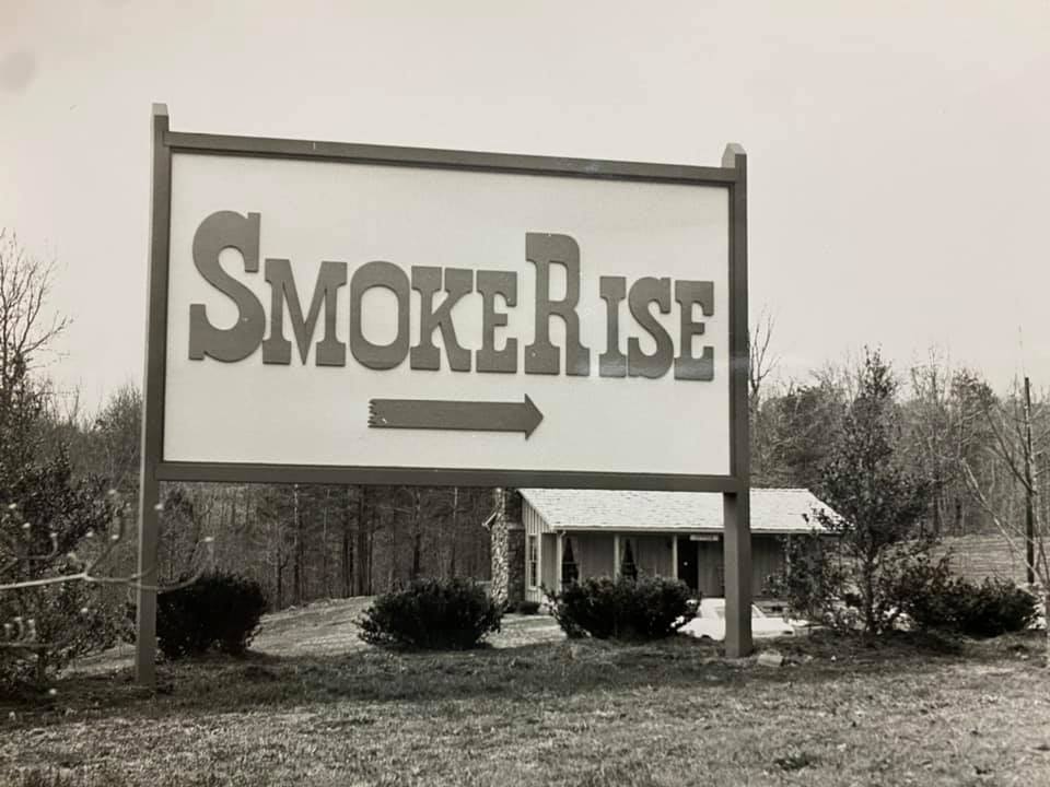 Black and white photograph of the original wooden Smoke Rise entrance sign, with an arrow pointing toward the subdivision entrance