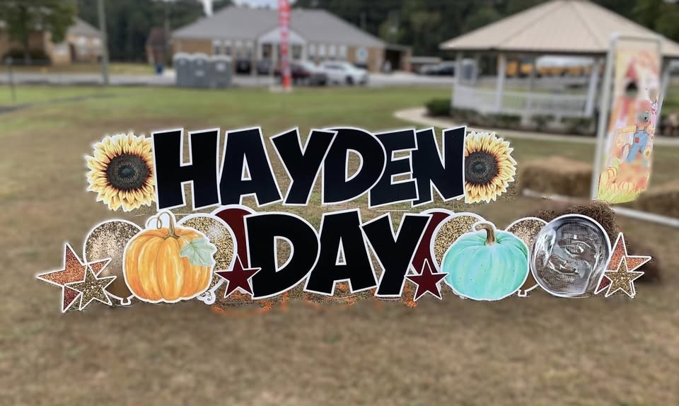 Black "HAYDEN DAY" lettering with sunflowers, pumpkins and stars on a lawn near the Hayden town hall park